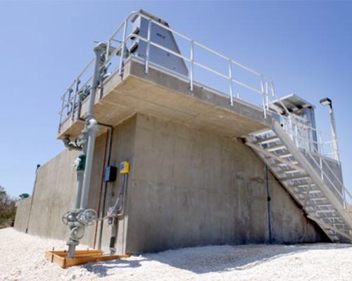 Looking up from ground level at concrete water treatment structure. Stairs lead up along the side..